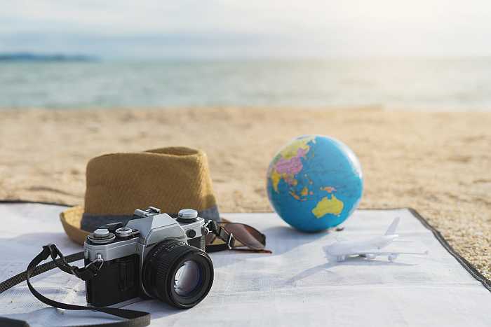 Travel items on a beach including a camera, hat, globe and toy airplane, symbolizing global Passover 2026 destinations.